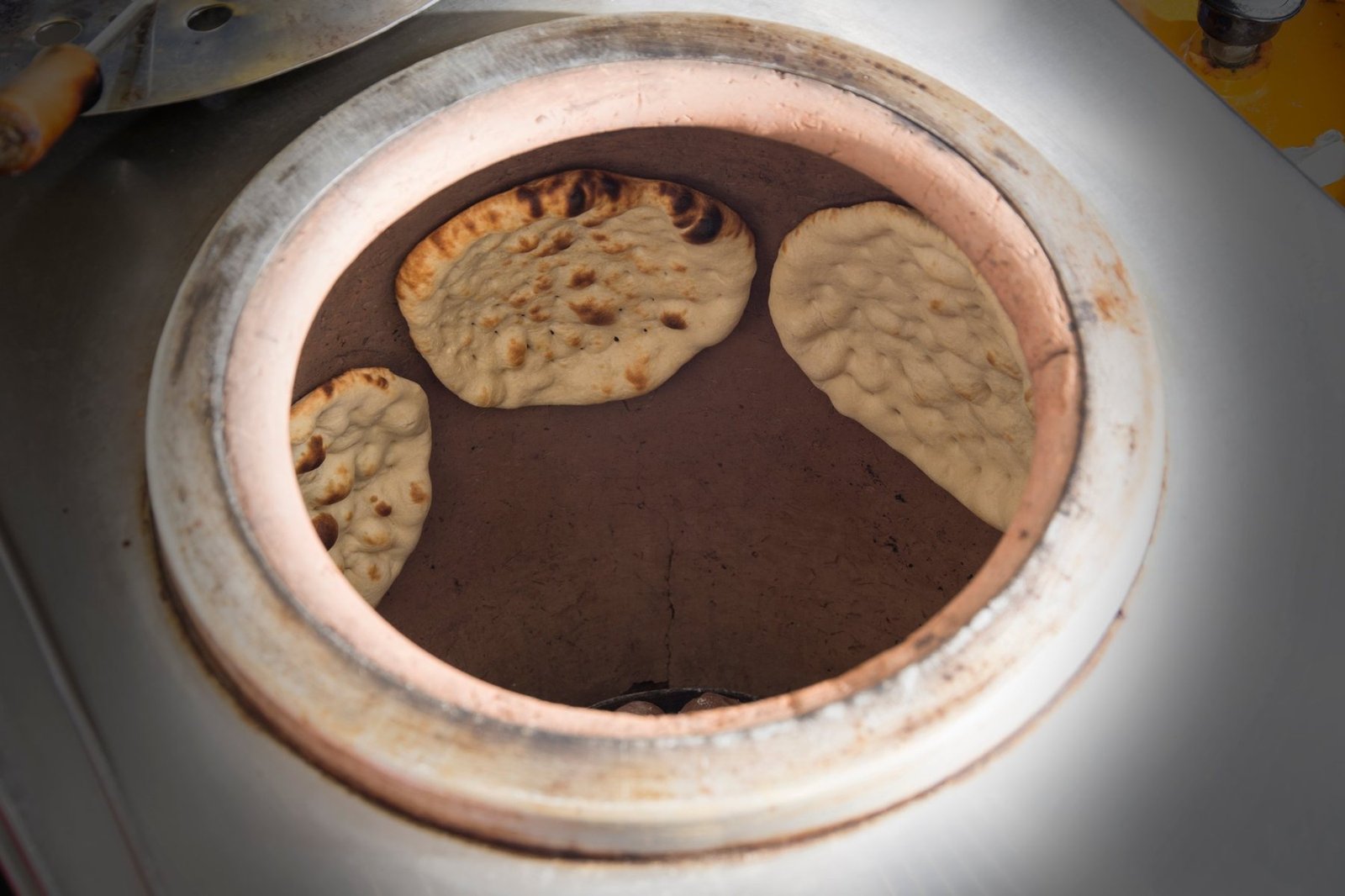 Tre naan klasket fast på lervæggen inde i tandoor-ovnen på Nørrebrogade 35, midt i bagningen