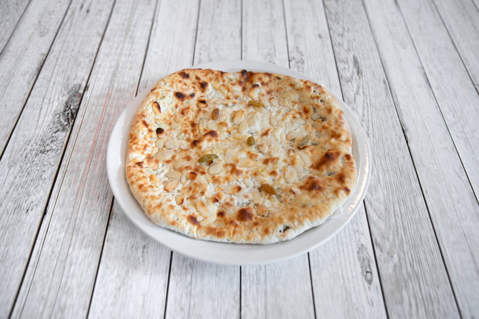 Peshwari naan — sødt fyldt fladbrød med mandelflager og rosiner, serveret på tallerken