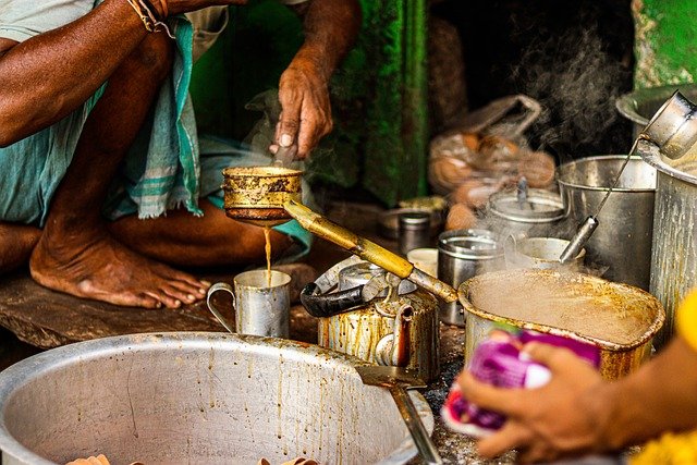 Autentisk billed fra indien hvor 2 kvinder som ikke kan ses laver indisk te som hedder masala chai. Kvinderne har lavet masala chai i en stor gryde, som de hælder op i små kopper.